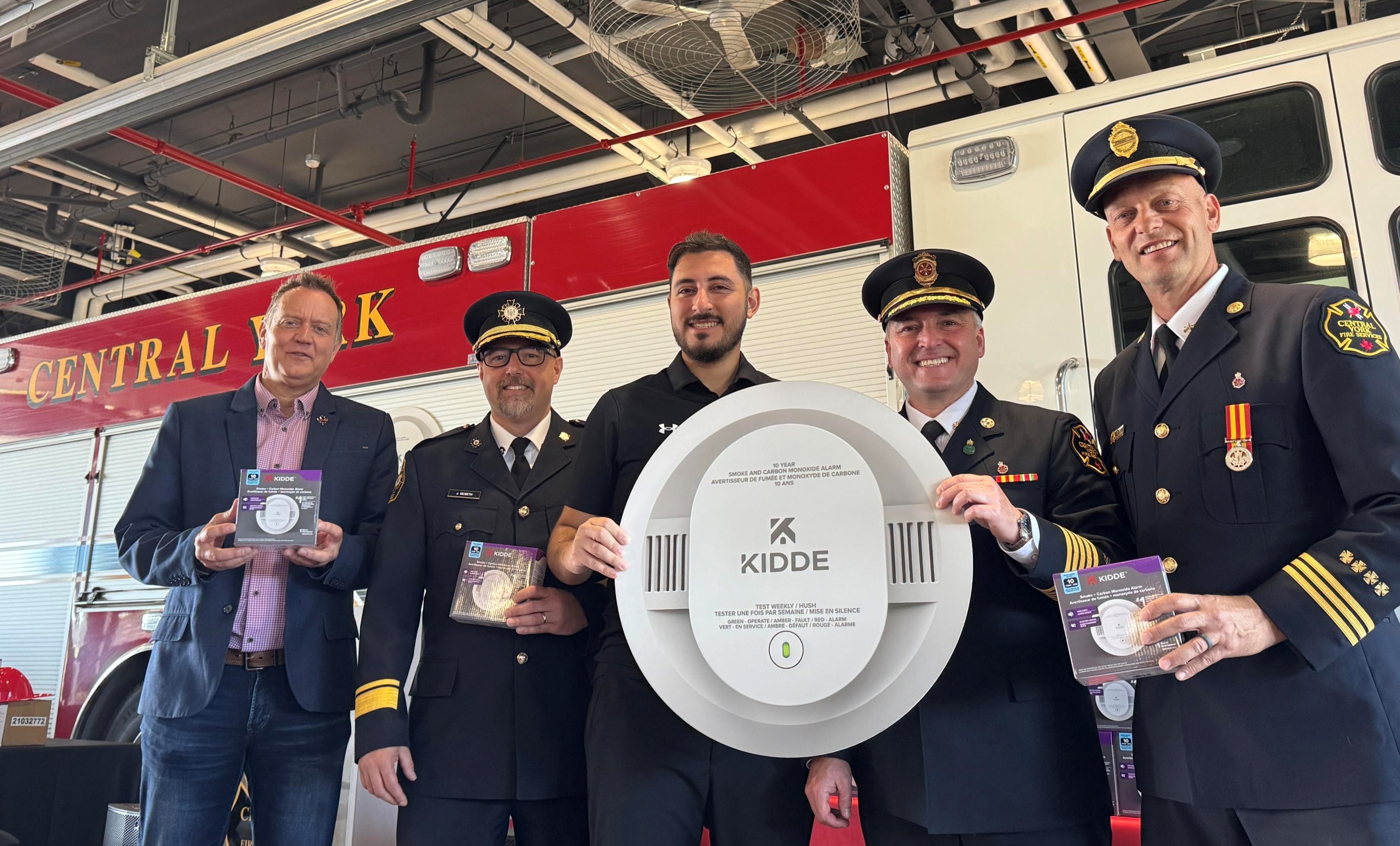 5 men in front of a fire truck, two holding up a KIDDE plaque