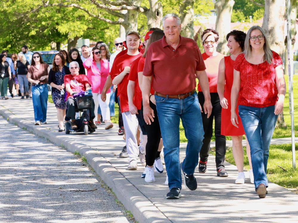 Participants, many wearing red, participate in a walk outside the County of Essex Administration Building.