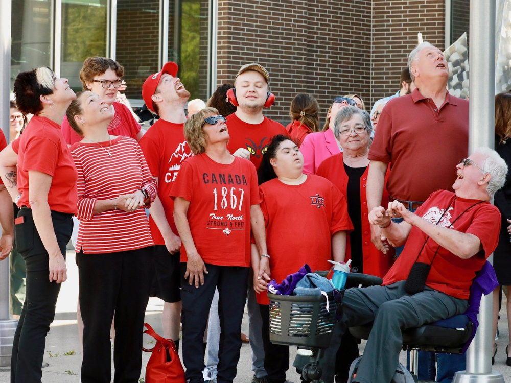Participants, wearing red, look up to see the flag atop the pole