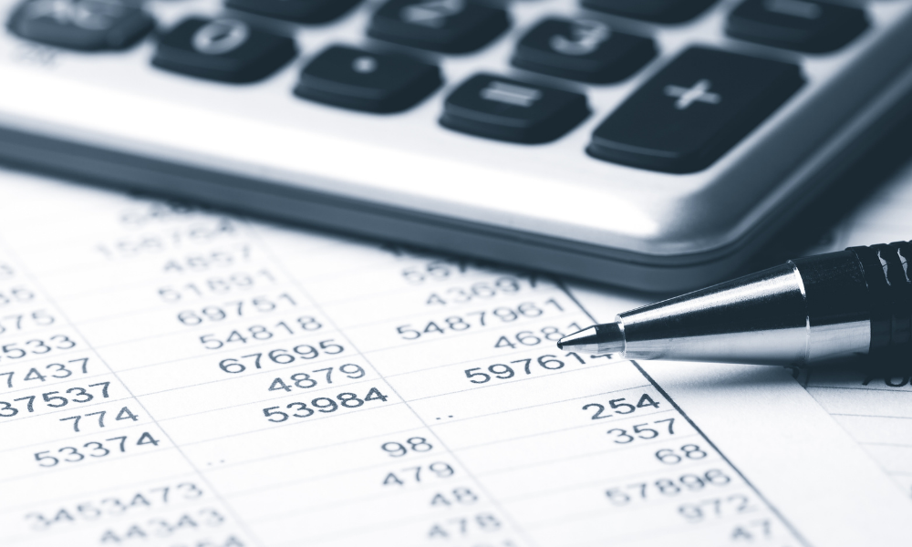 A spreadsheet with figures under a calculator and pen.