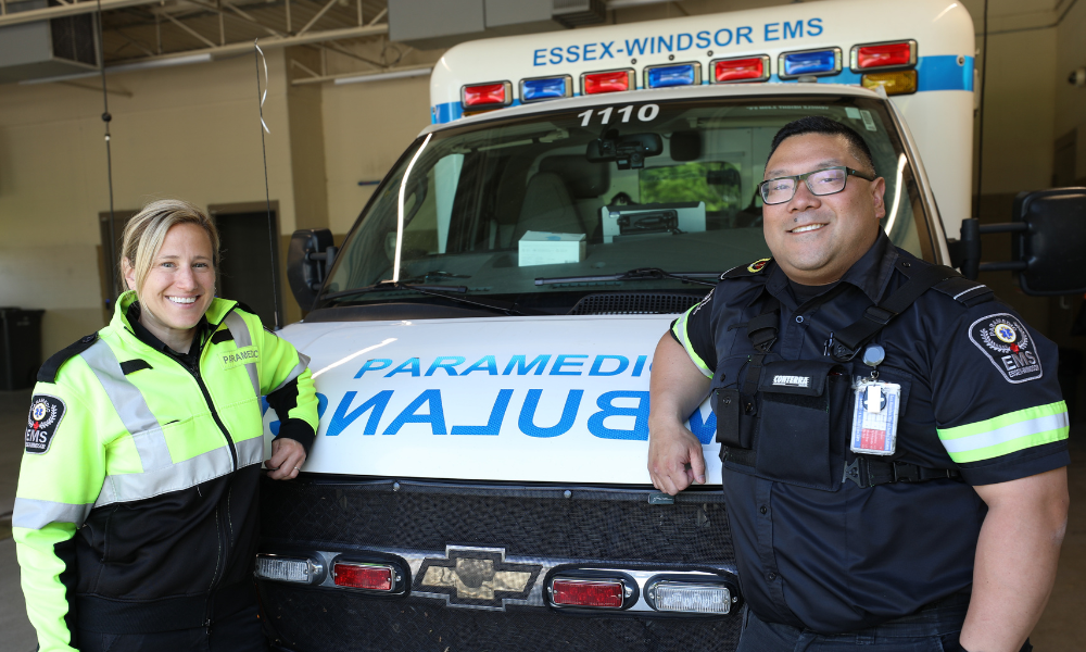 Two paramedics standing in front of an ambulance at their station.