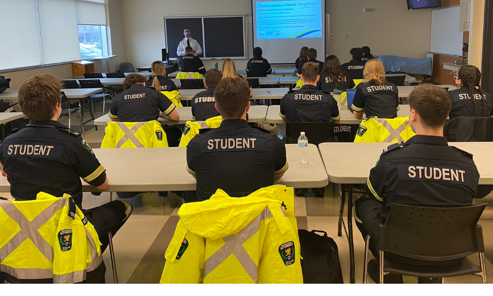 Paramedic students in a classroom listen to an instructor.