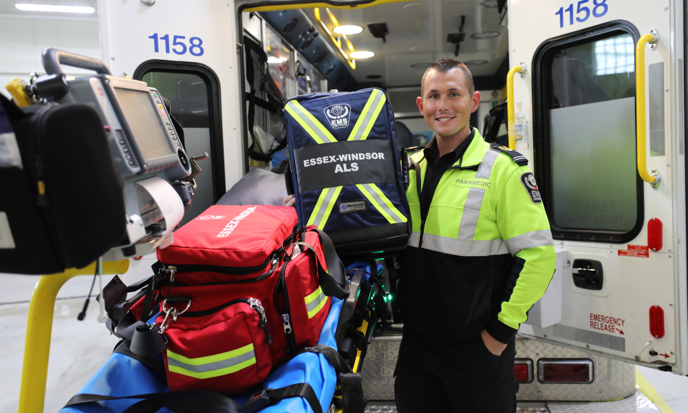 An advanced care paramedic stands at the back of an ambulance with a stretcher and other equipment he uses.