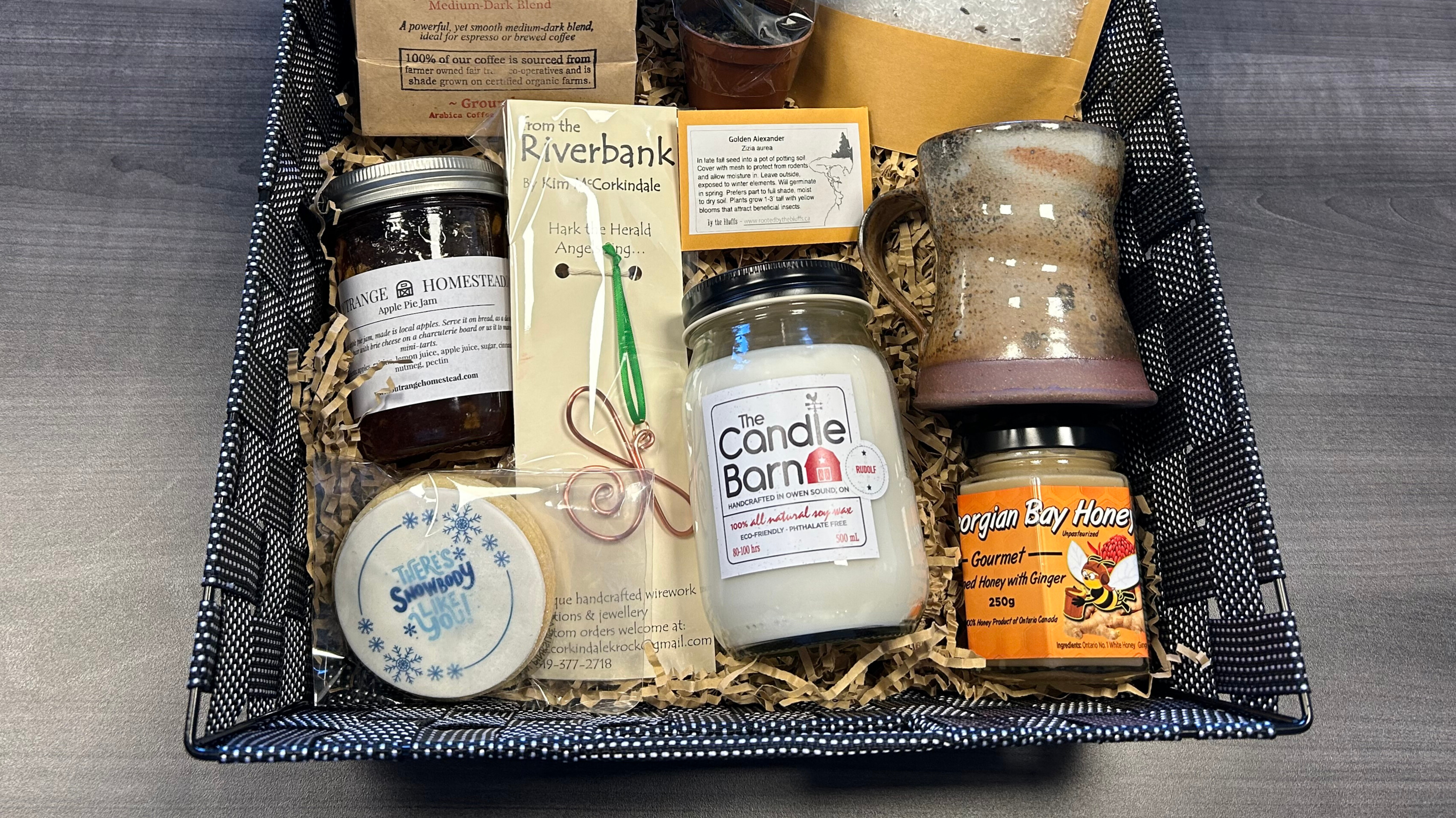 A basket of local products including a mug, candle, coffee, bath salts, ornament, and more