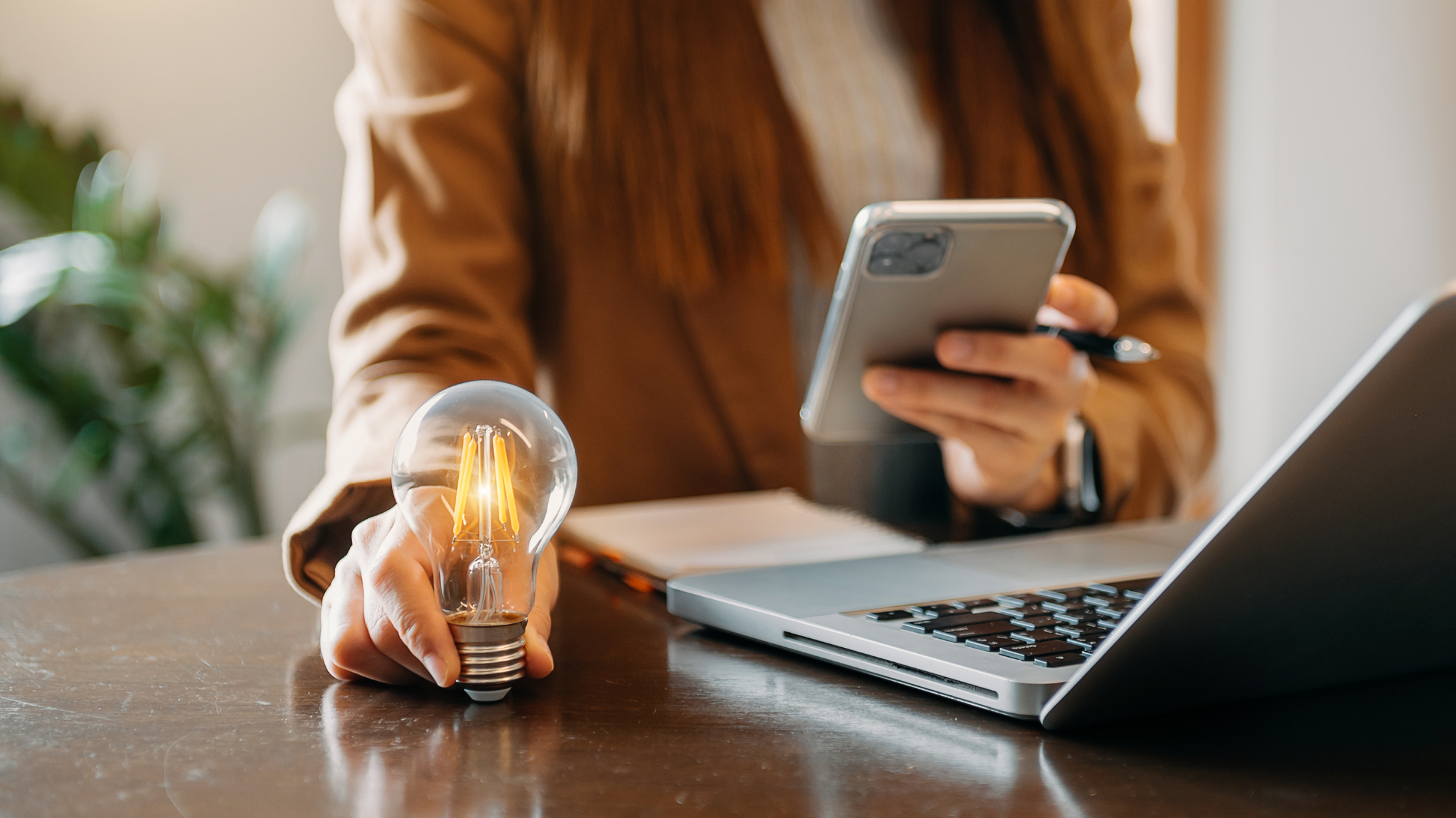 hand holding a lit lightbulb while scrolling a smartphone