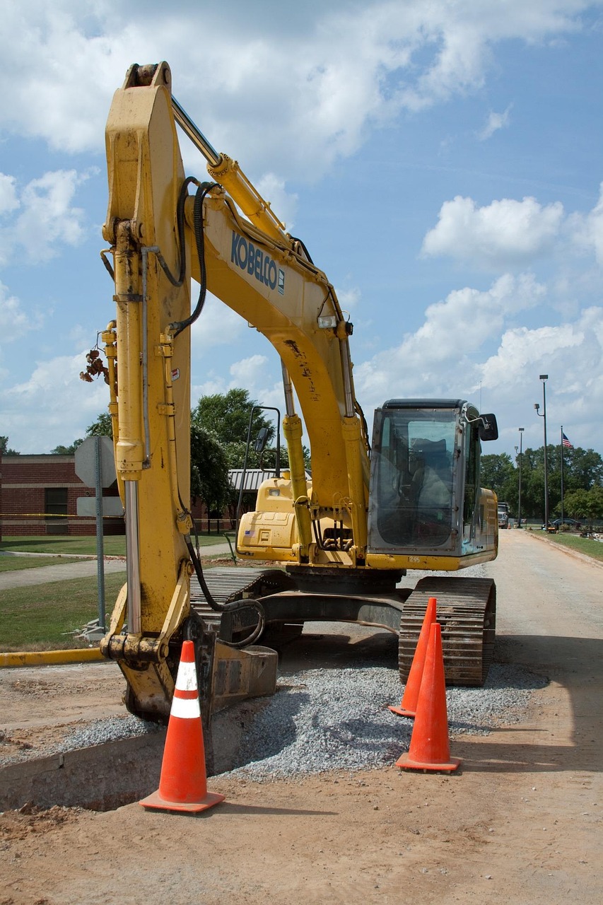 excavator with arm down next to a pit surrounded by pylons