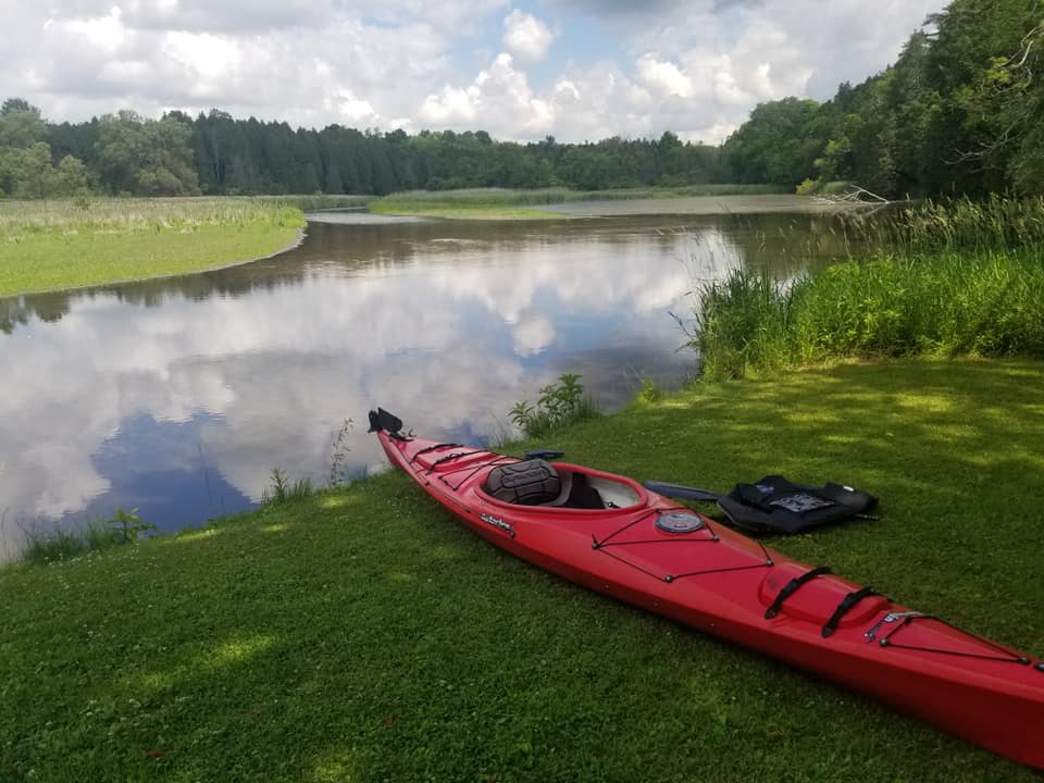 red kayak sitting on the side of a river with many trees in the background