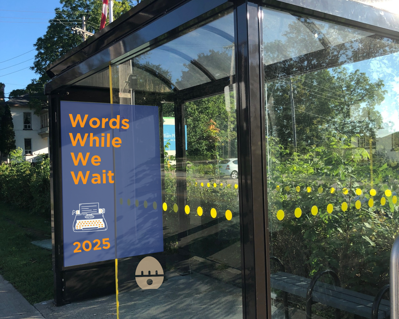 Bus shelter with a blue poster displaying the words "Words While We Wait 2025." Also on the poster is a typewriter graphic.