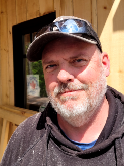 Adult male with white beard, wearing hoodie, baseball glasses and ball cap.