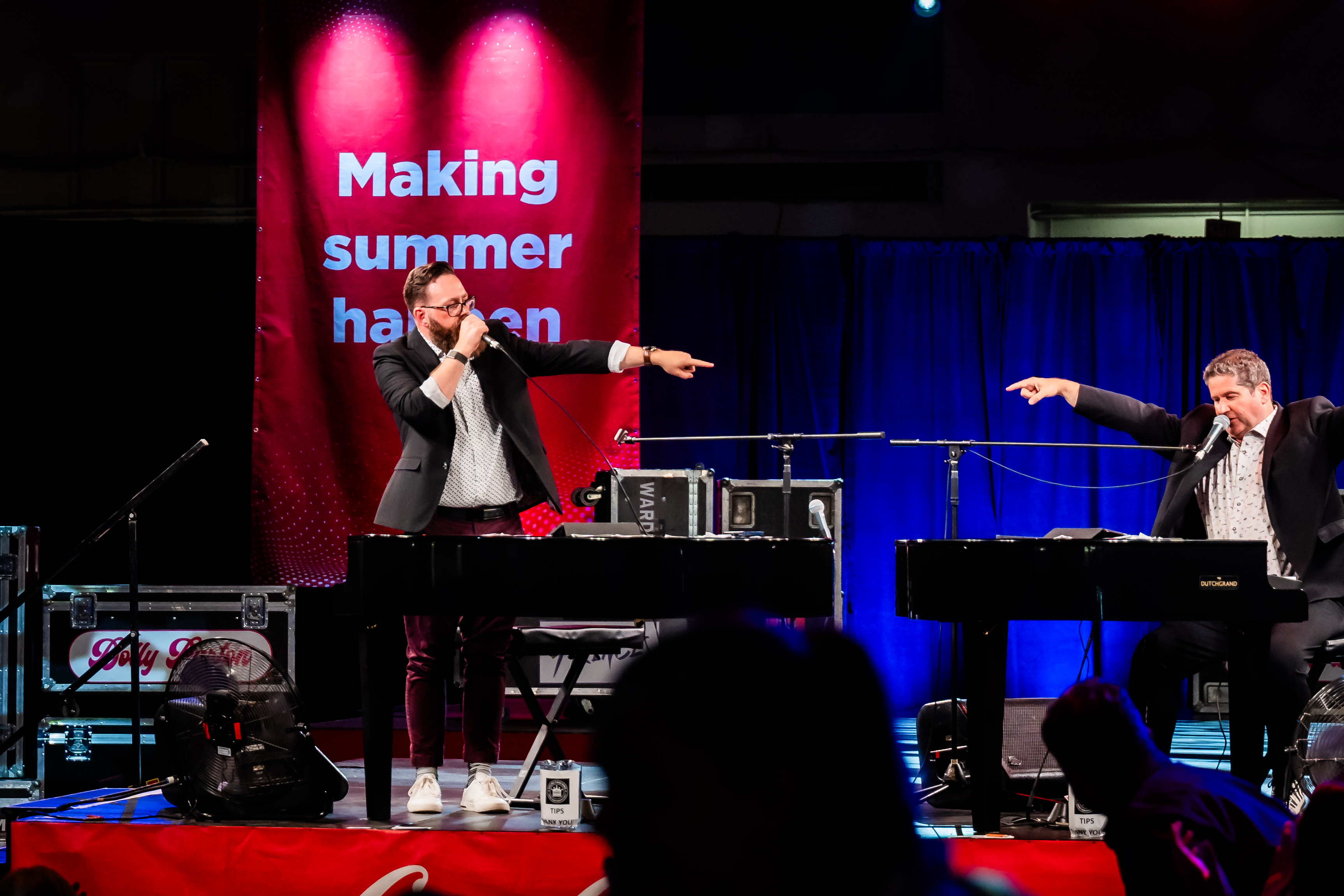 Two performers entertaining the audience on stage with dueling pianos during a live event.