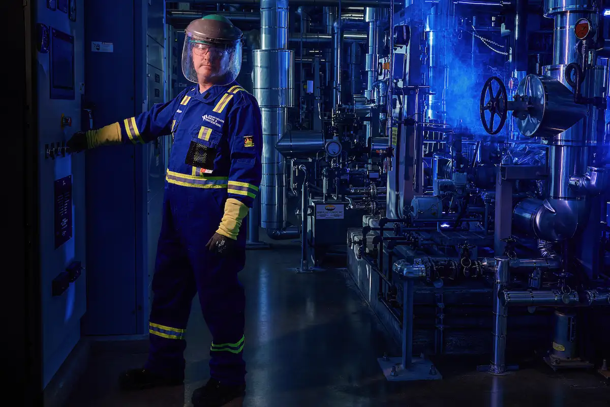 Power engineer standing beside industrial control equipment inside a processing facility.
