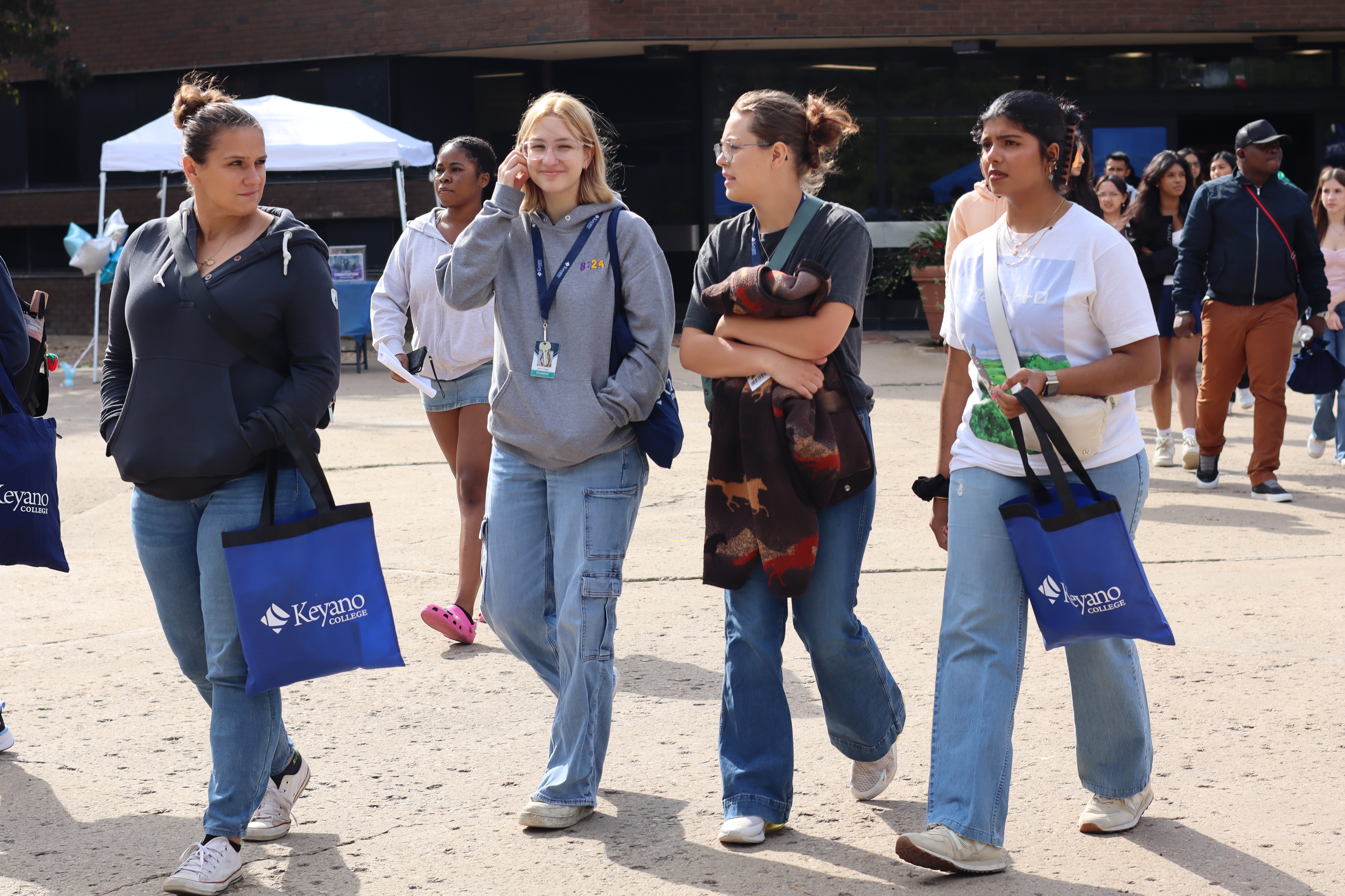 Four students walking holding Keyano tote bags