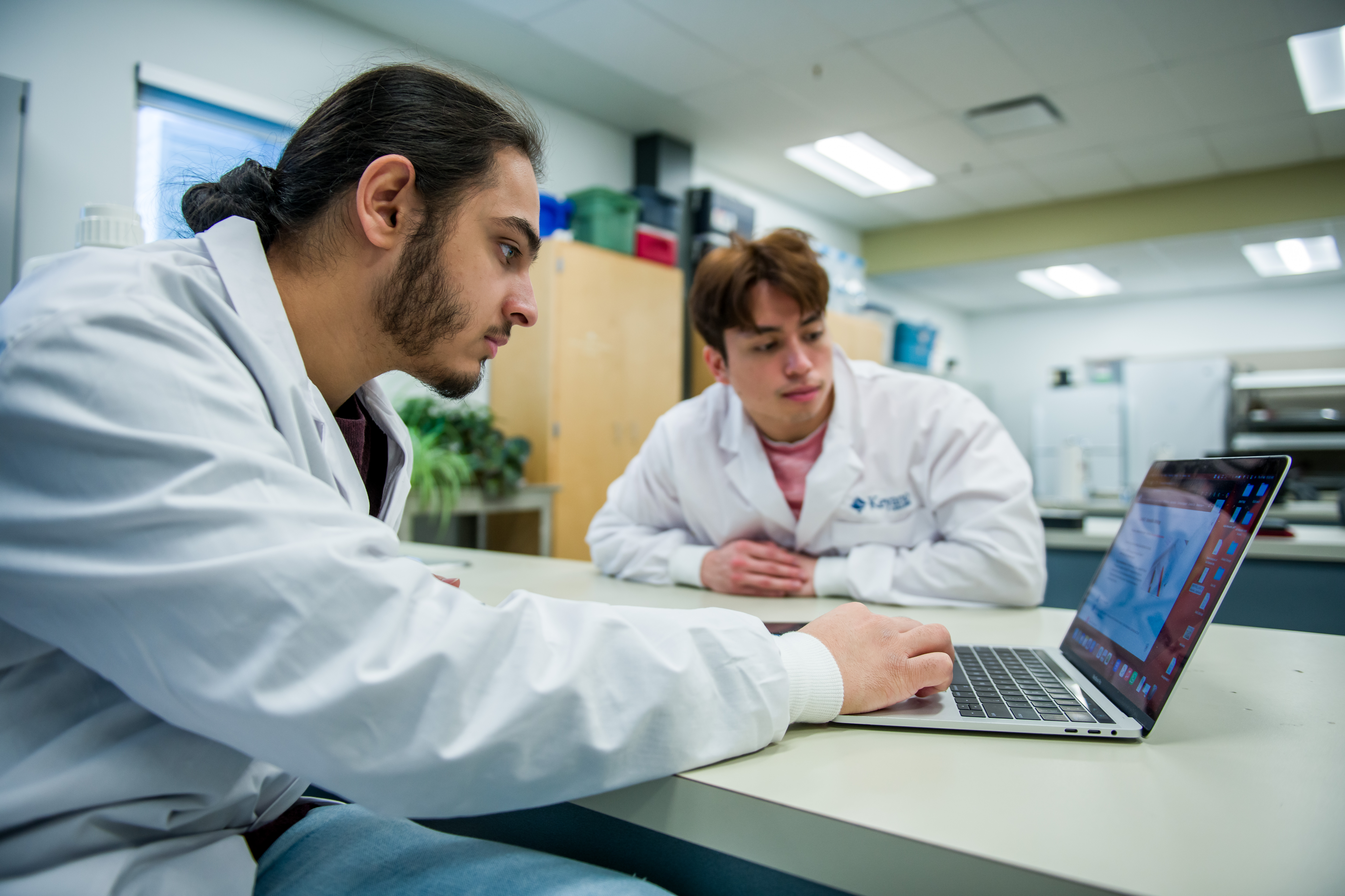 Two students wearing lab coats looking at a laptop 