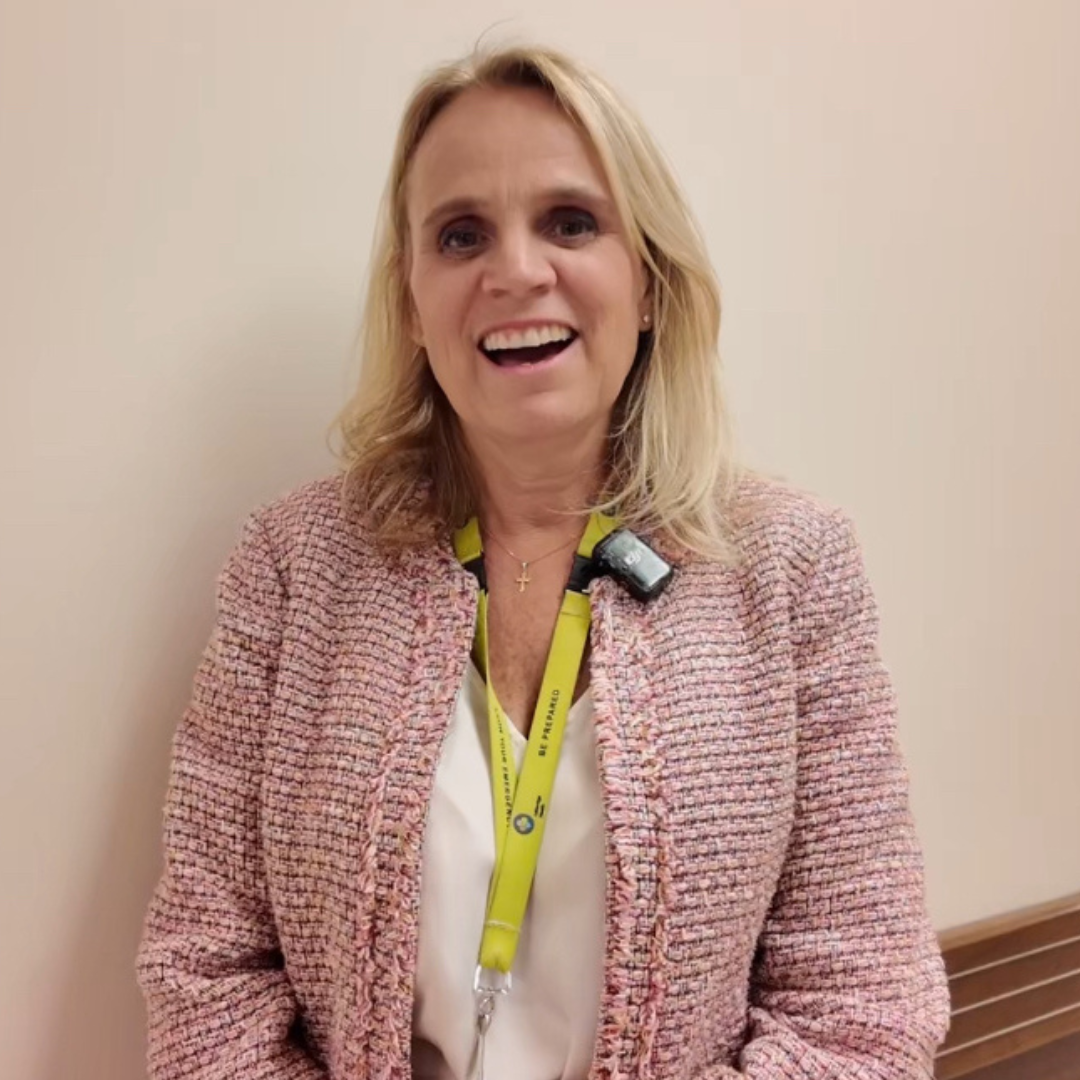 A woman with blonde hair stands in a hallway, smiling.