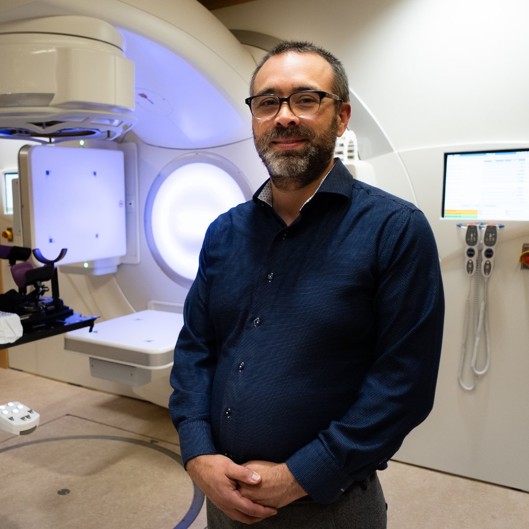 Dr. Joel Broomfield stands in front of radiation therapy machine.