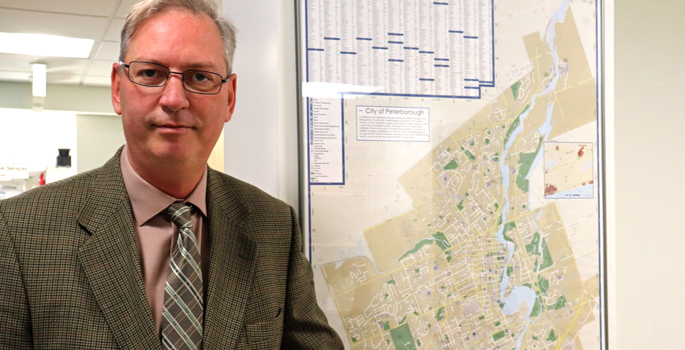 headhot style photo of Richard Freymond including City of Peterborough Map beside him.