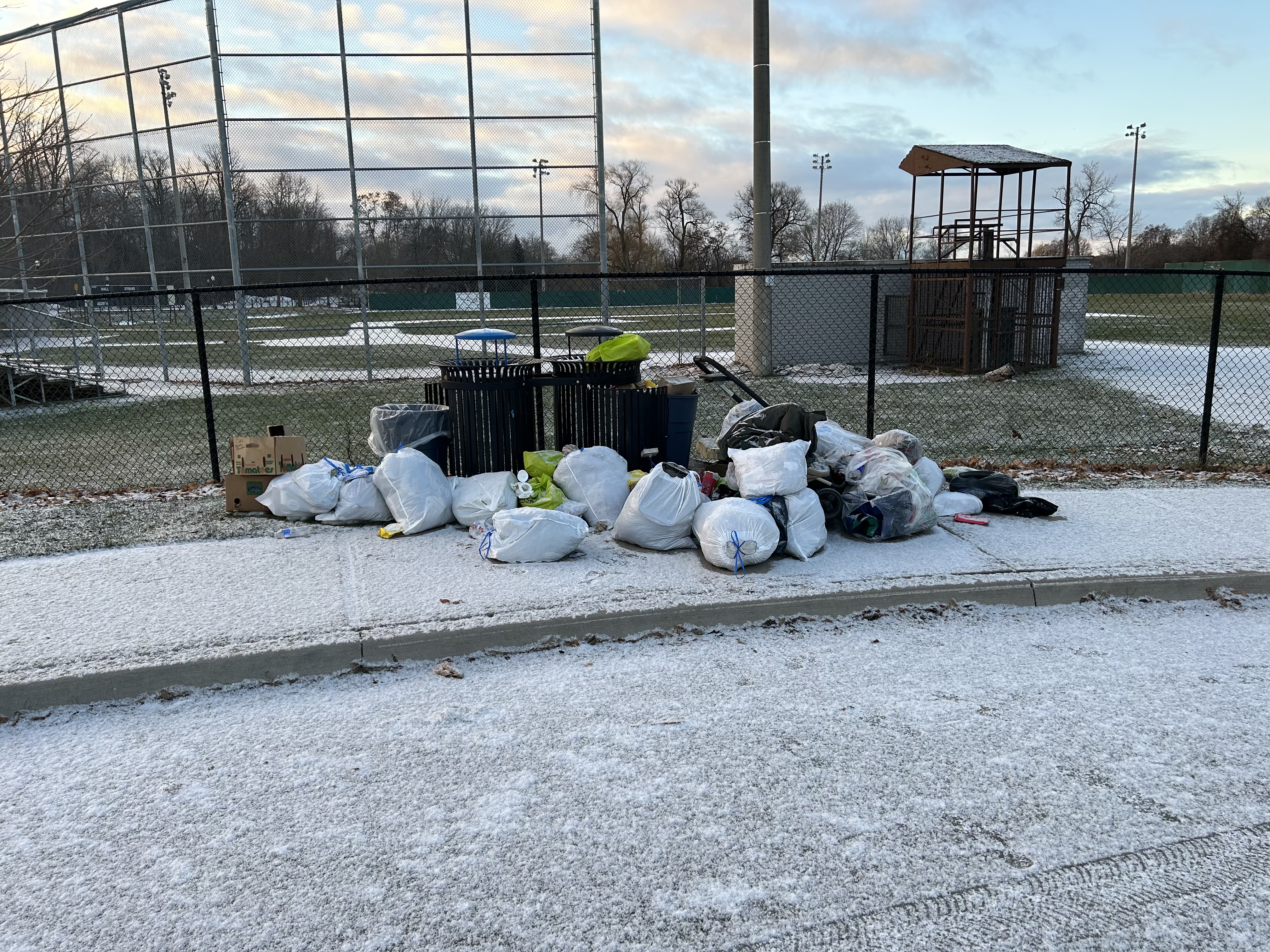 Park garbage and recycling cans with a pile of bags of garbage surrounding them.