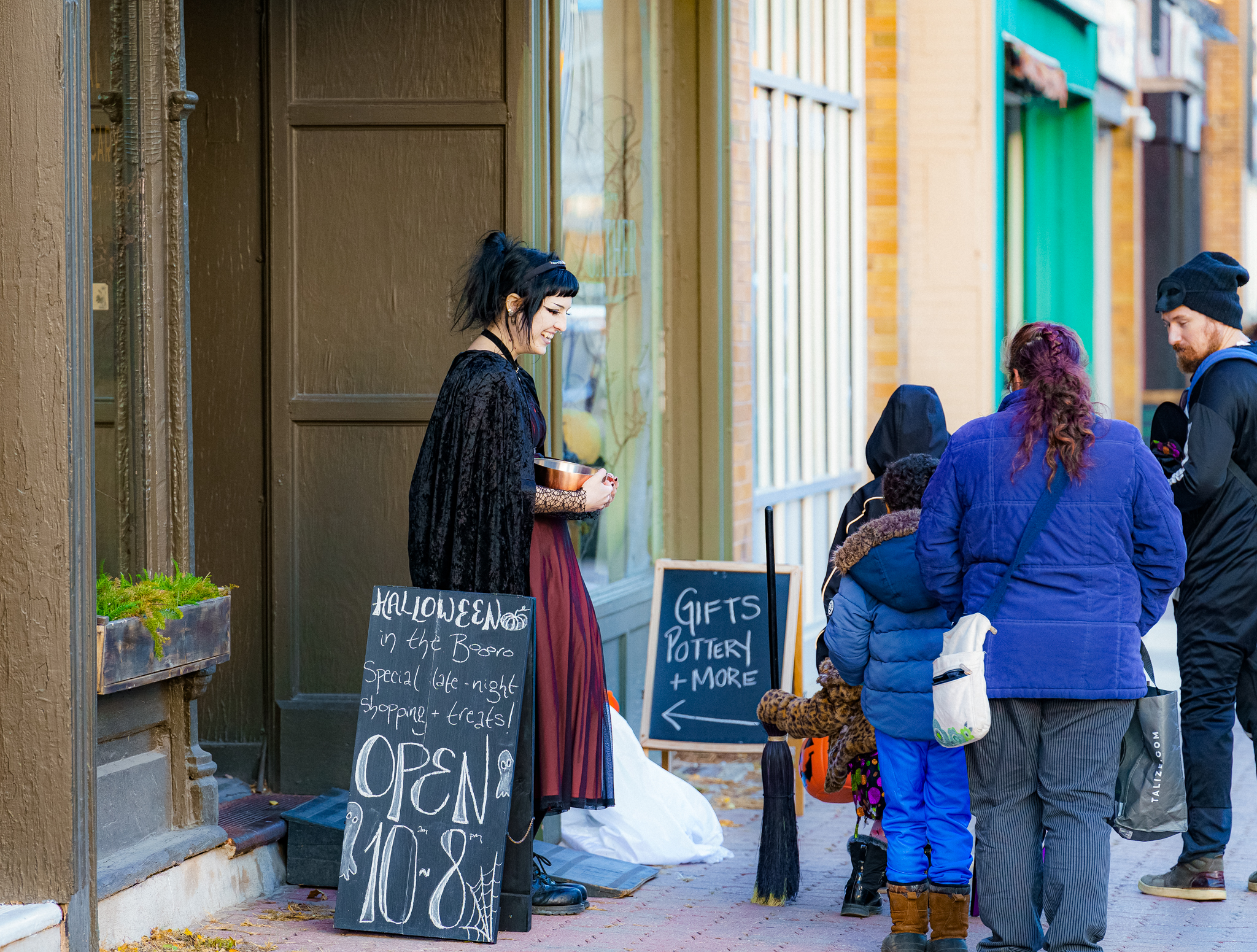 A person dressed in a witch costume hands out candy to trick or treaters in downtown Peterborough.