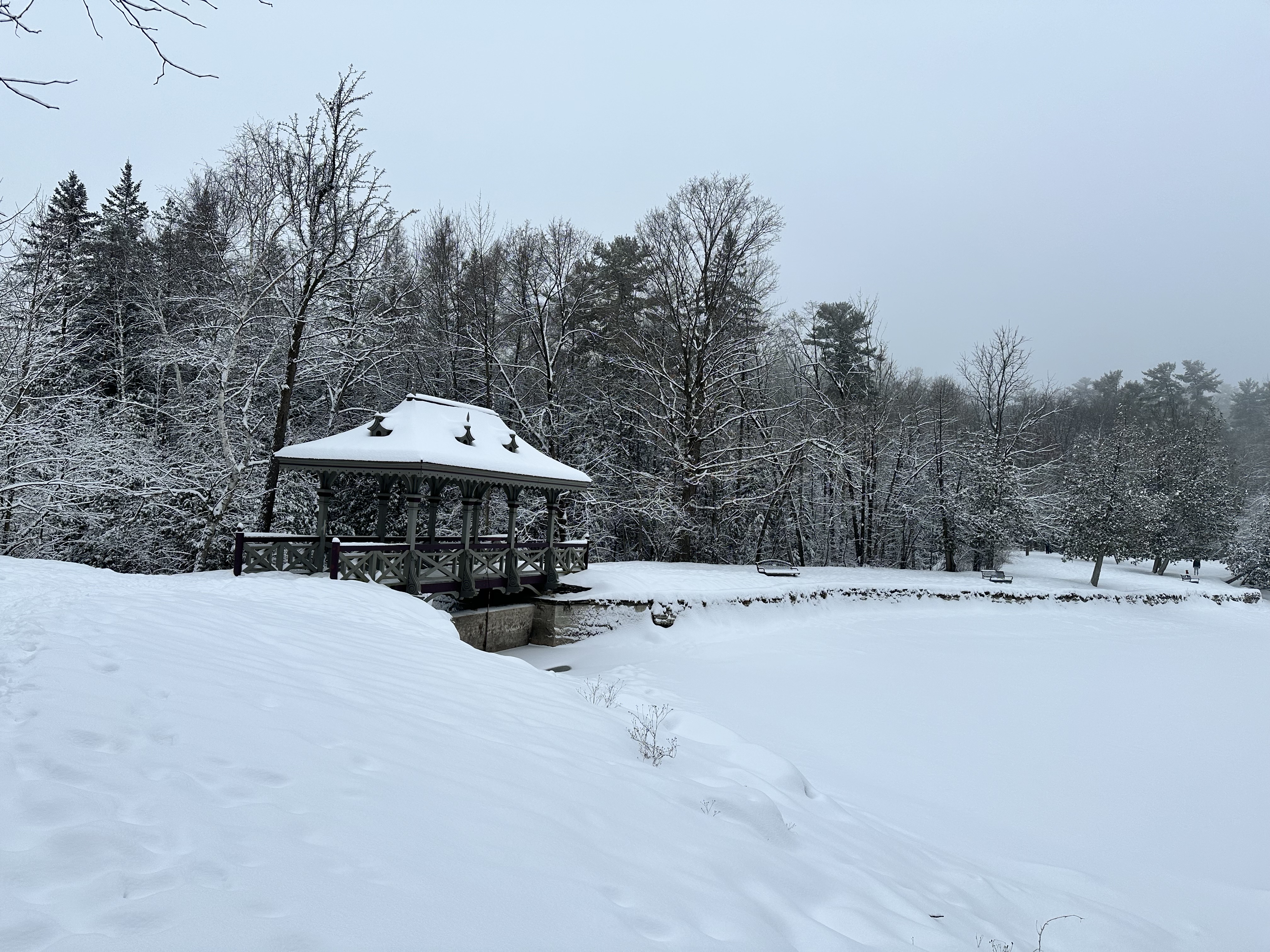 A covered walking bridge crossing over a stream covered in a large amount of snow.