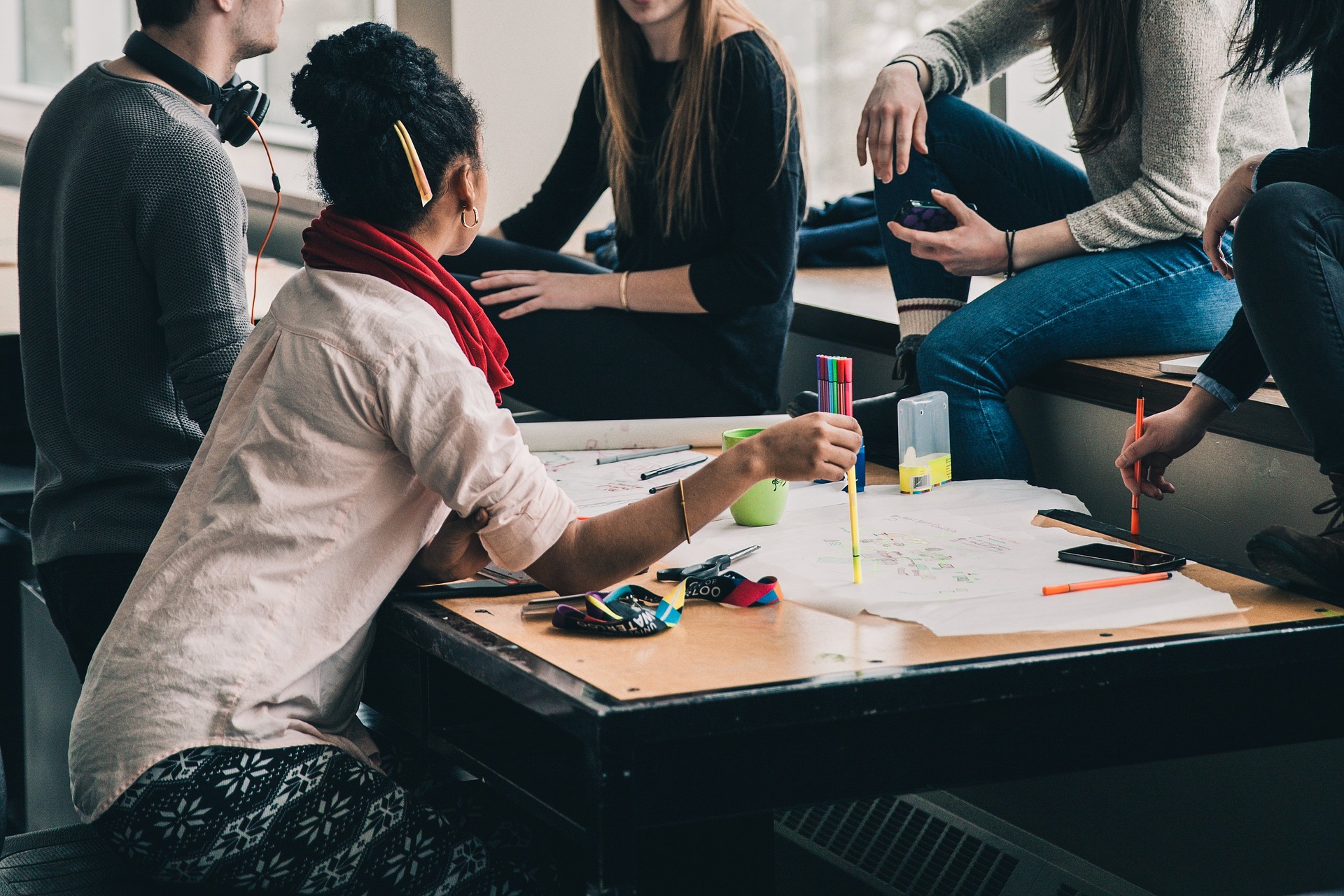 Woman with headphone on sitting a table with others working on a group project.