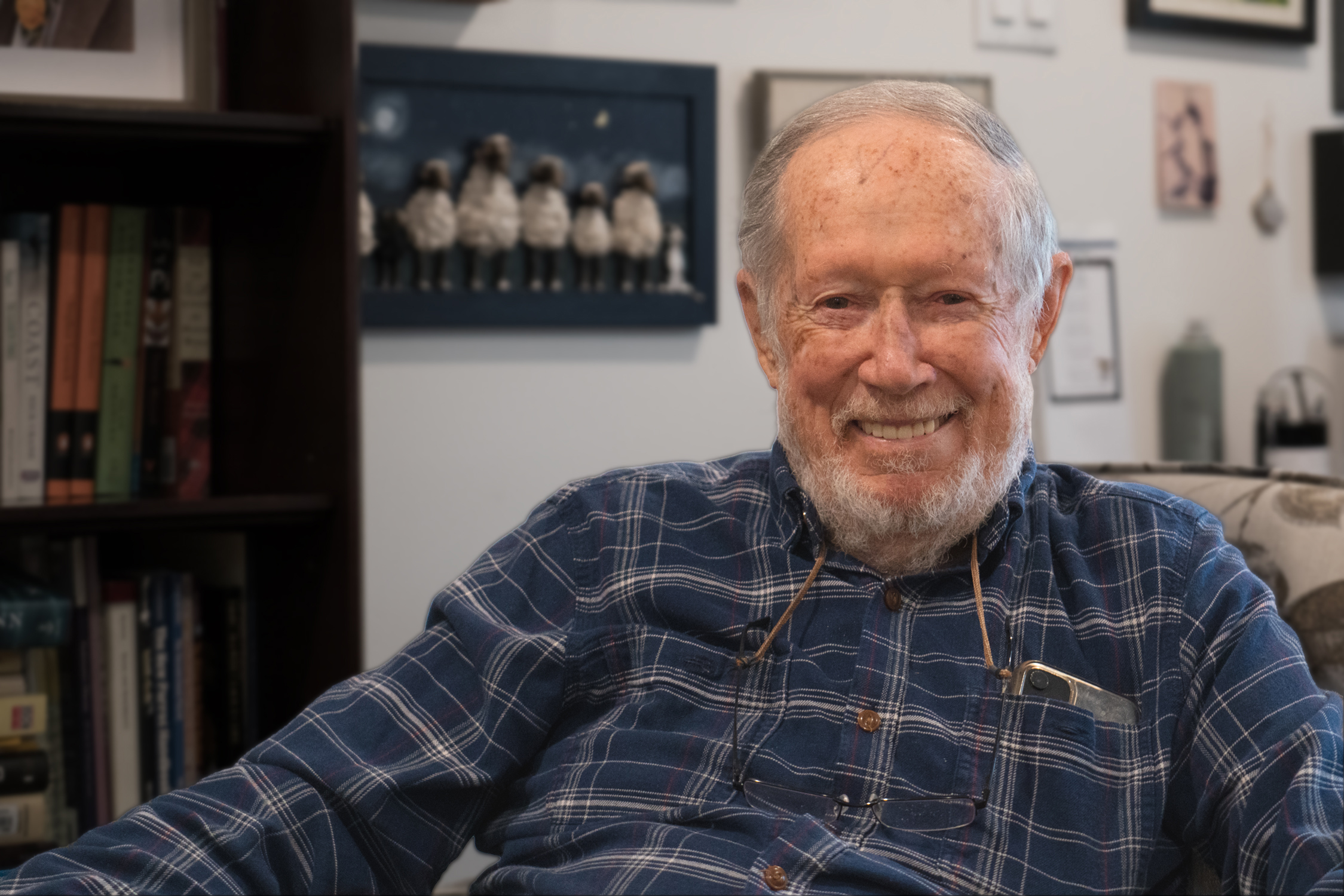 An older gentleman with a white beard and wearing a dark plaid shirt smiles at the camera