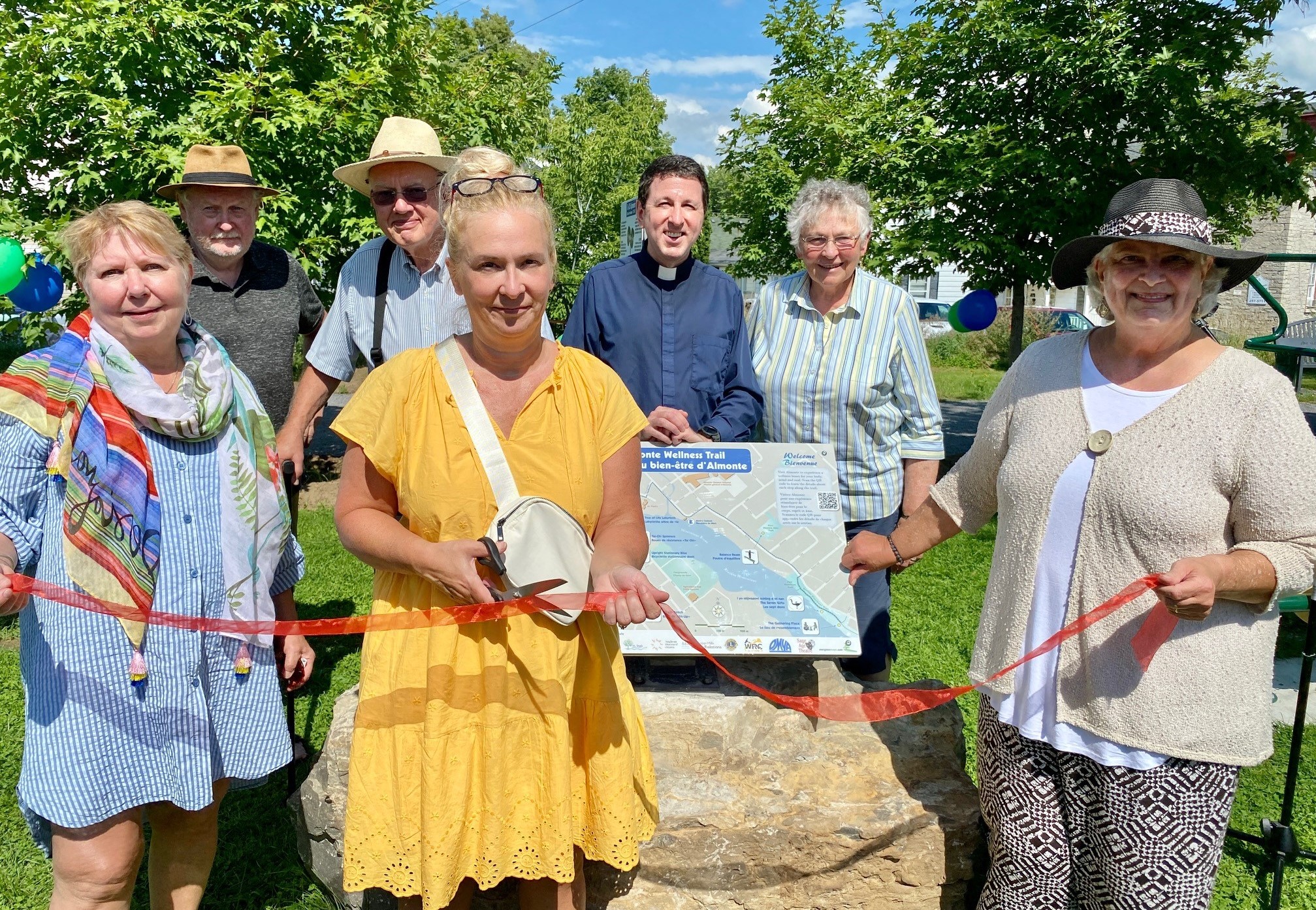 Three people surround a large rock holding a ribbon while four people stand behind