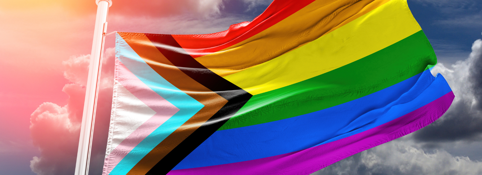 The Progress Pride flag waves against a blue sky