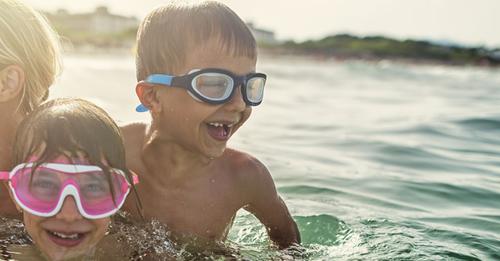 Three kids wearing goggles swim in water on a sunny day