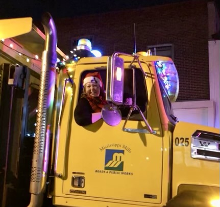Woman wearing a Santa hat sits in the passenger seat of a yellow plow truck