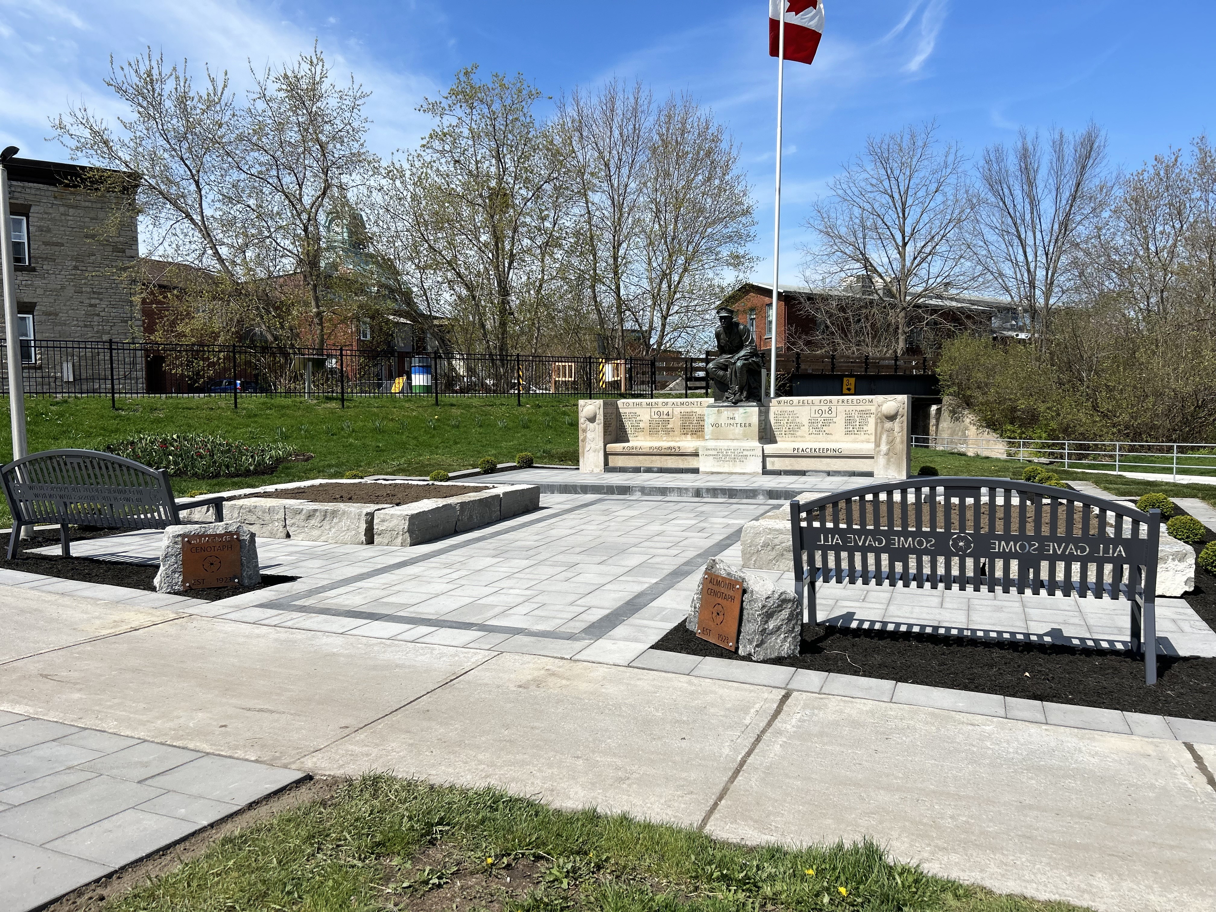 Photo of bronze statue surrounded by light grey stone and flower beds