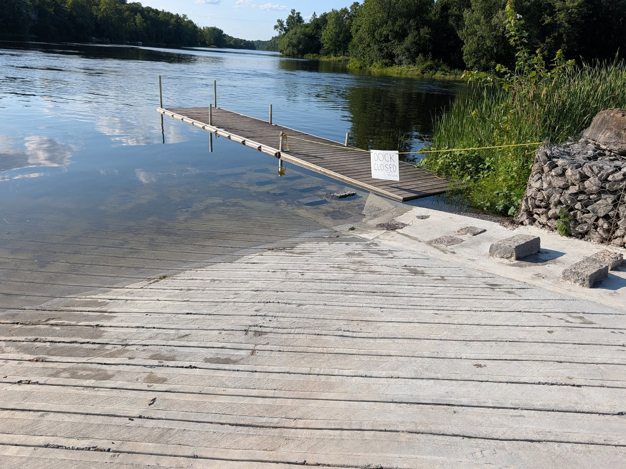 A dock is nearly submerged by high water levels at a boat launch by a river