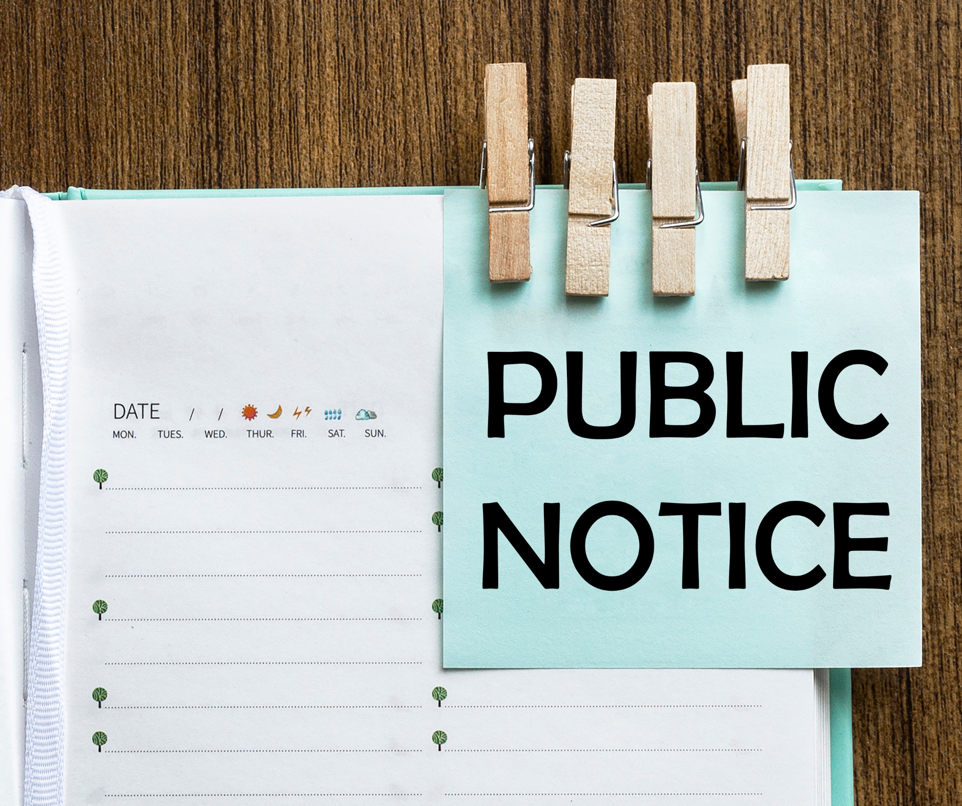 Image showing open agenda book on a wooden desk with a note reading 'Public Notice' pinned to the book with clothespins.