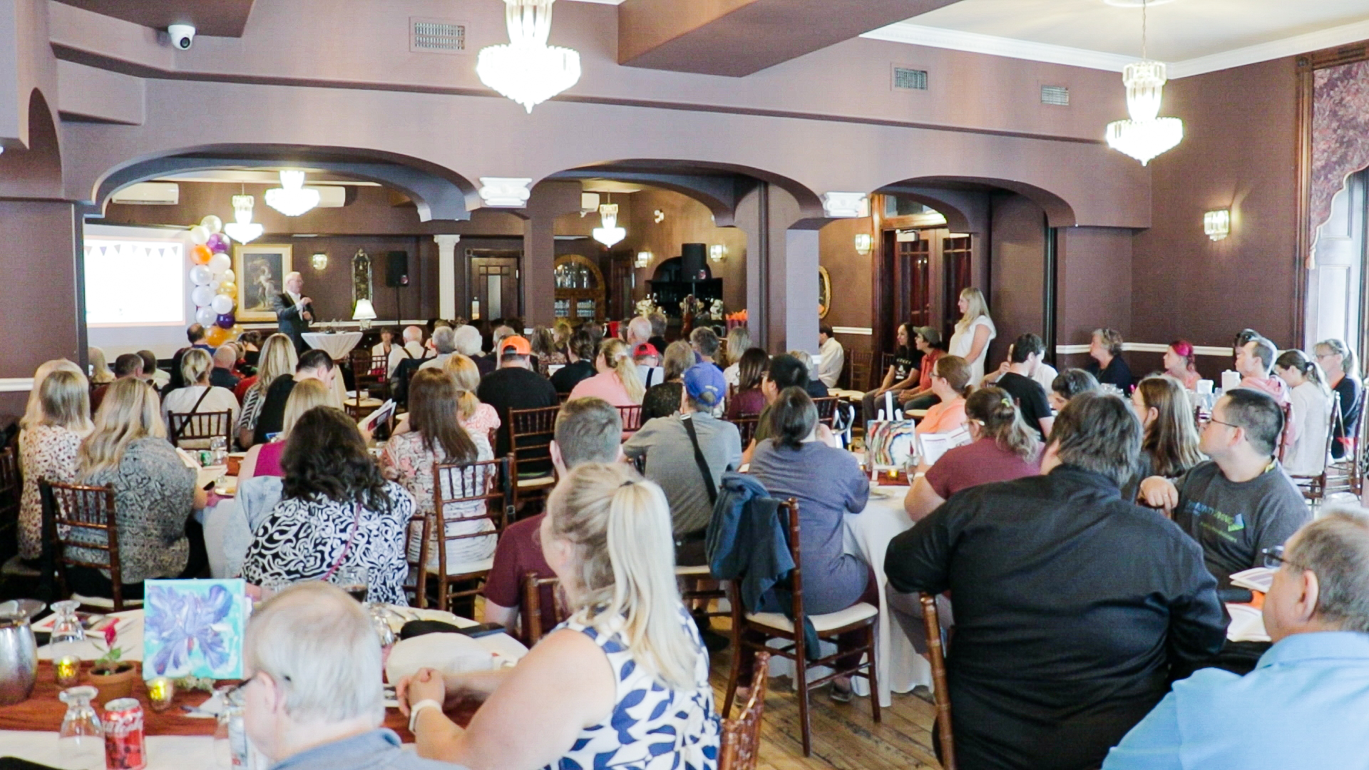 Large group of people inside a hall seated at tables.