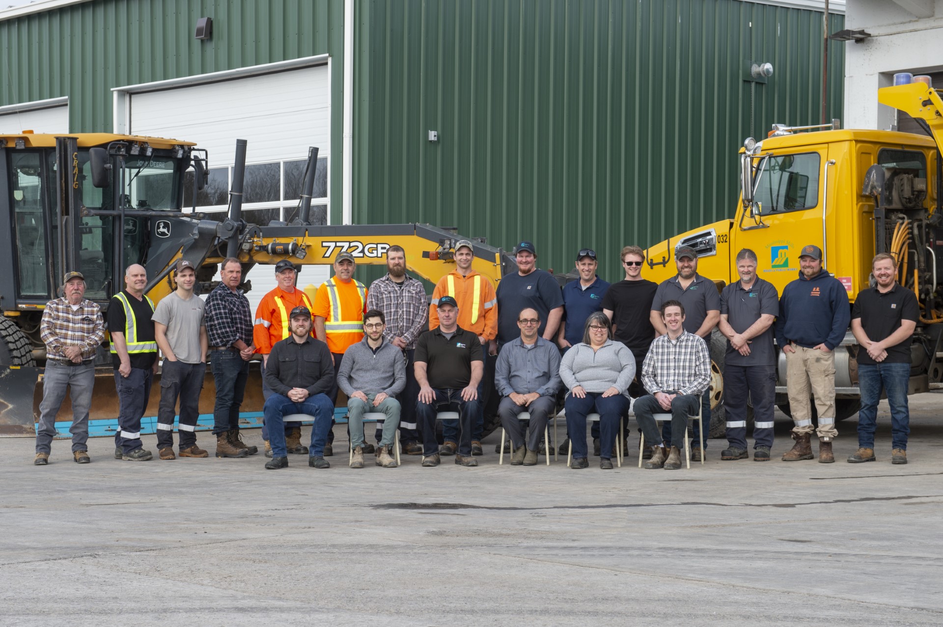 Photo of group of people standing in front of large pieces of yellow road equipment
