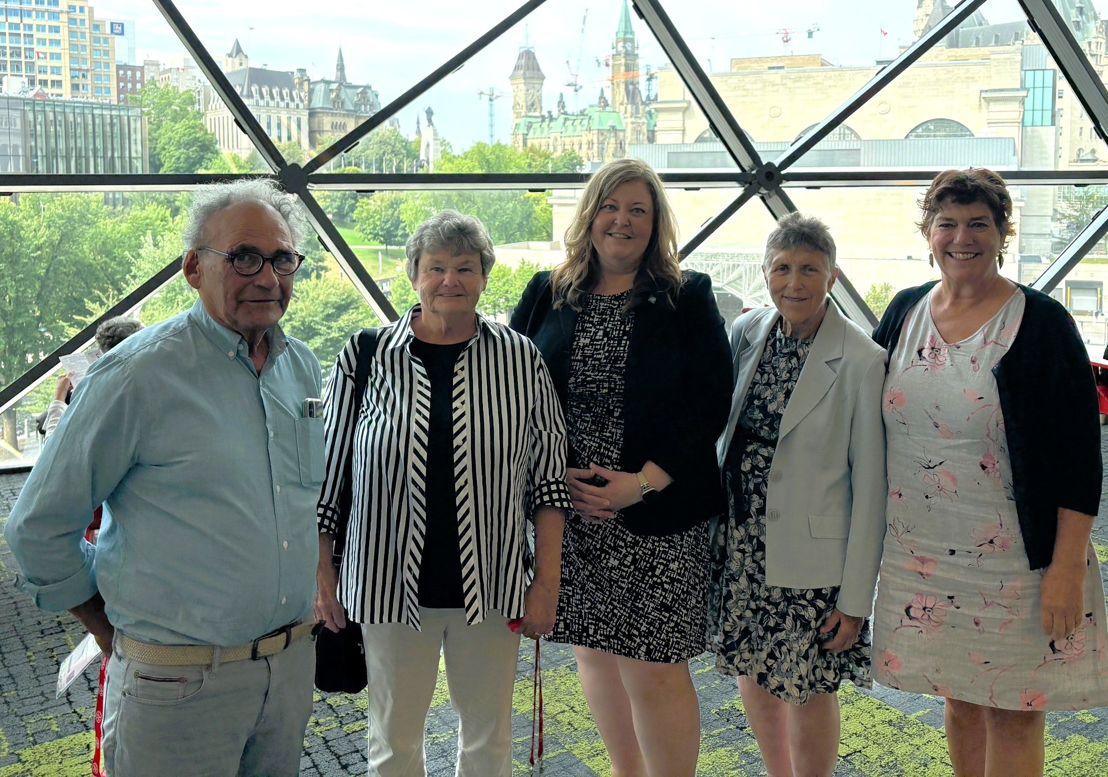 Five people stand in front of a bank of windows for a photo