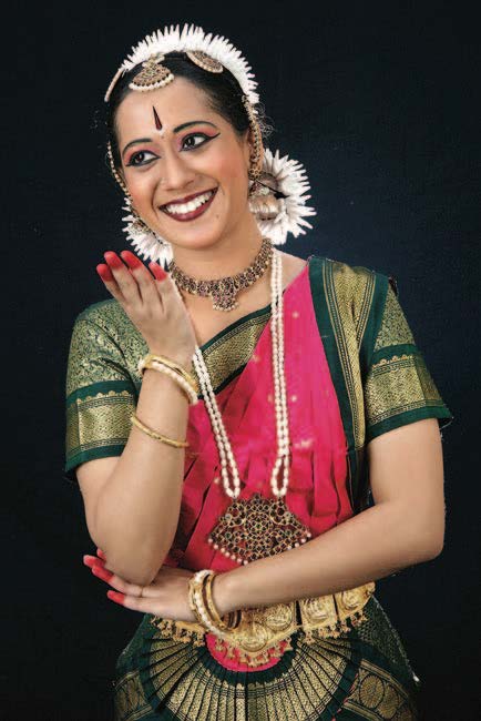 Dark haired woman in gold, green and pink dress poses for a photo with arms raised