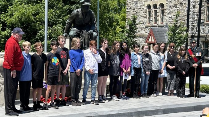 A large group of people stand outside in front of a stone war memorial
