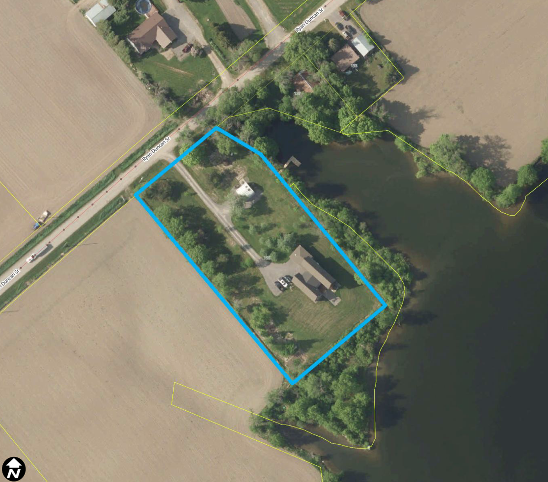 Satellite view of rural area surrounded by forests and agricultural fields. A property is outlined in blue.