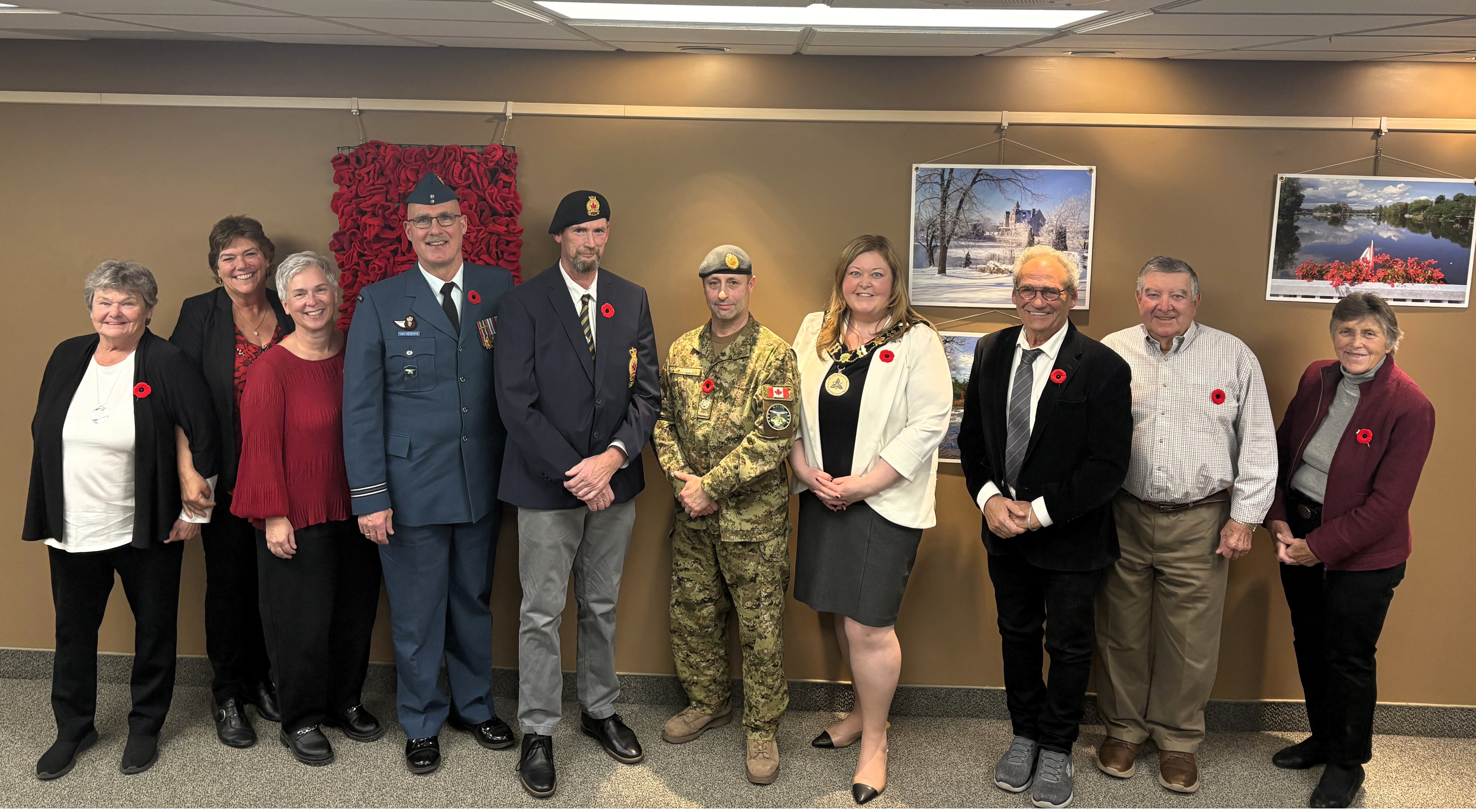 People and veterans standing in front of a poppy display and photos on a beige wall