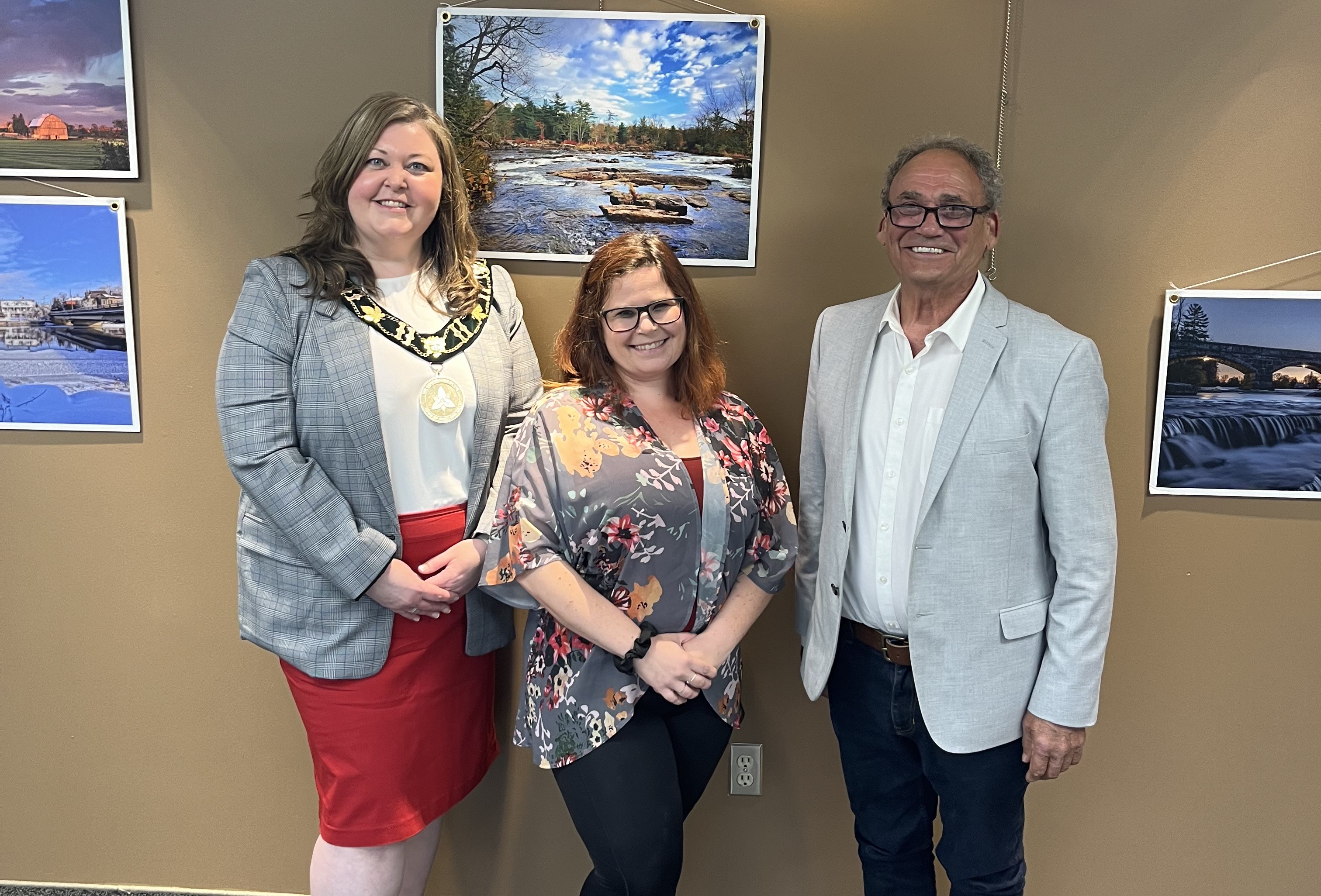 Three people stand in front of photographs on a beige wall