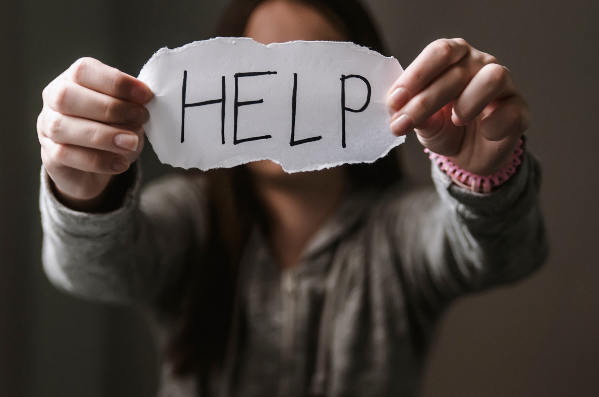 Person holds a handwritten note in front of them with the word 'Help' written on it