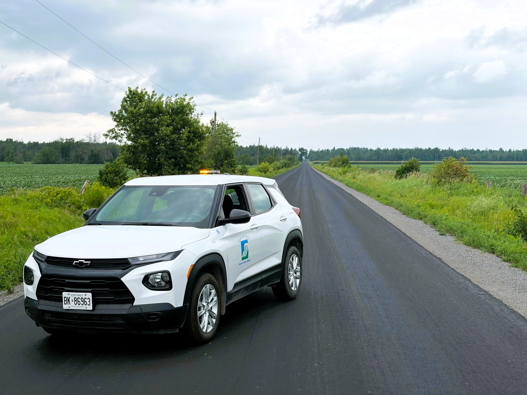 A white SUV is parked along a freshly paved road in a rural area