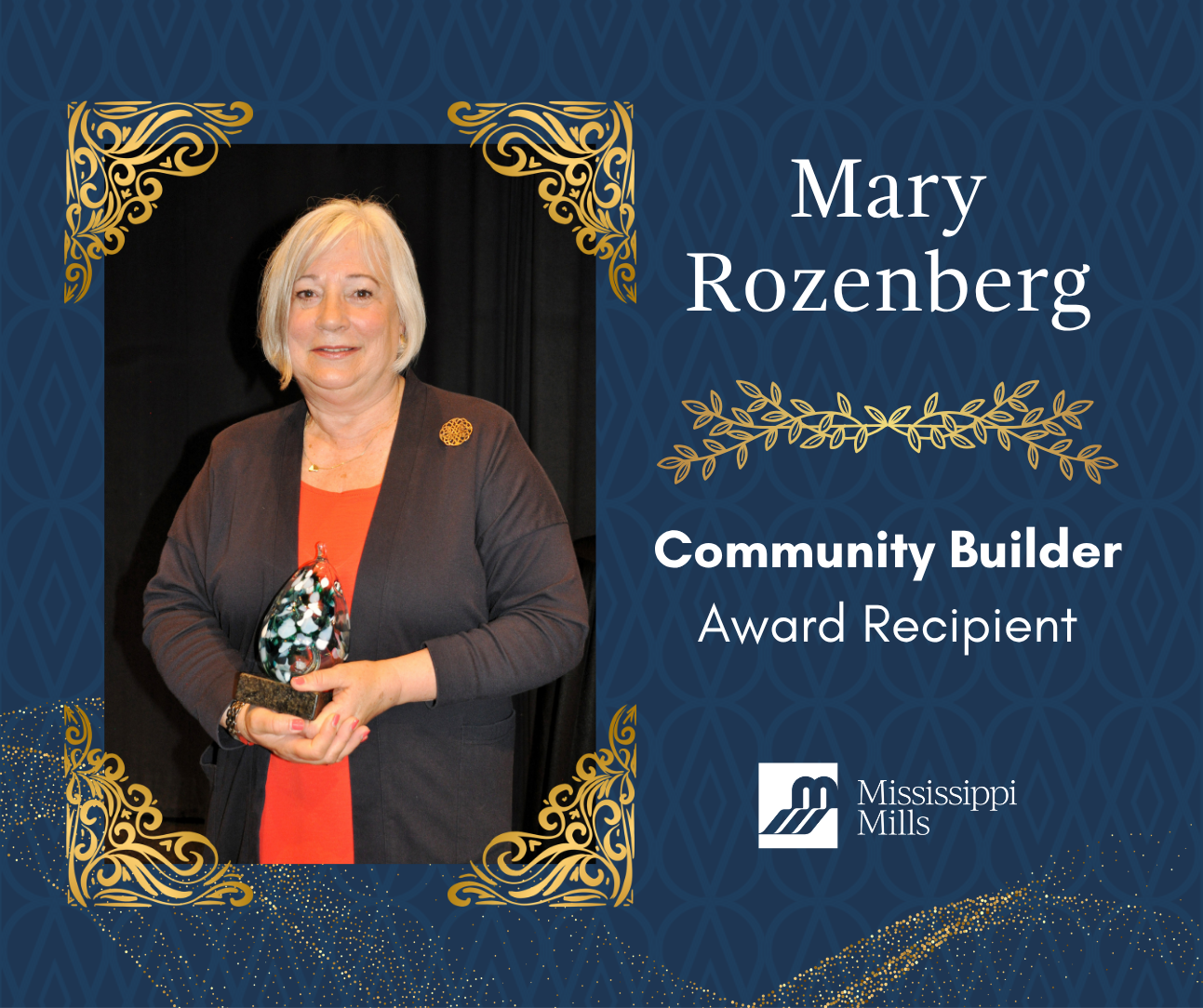 Navy background with gold accents. A woman with a silver bob, wearing a dark blazer and red dress smiles while holding an award. White text reads 'Mary Rozenberg - Community Builder Award Recipient.'