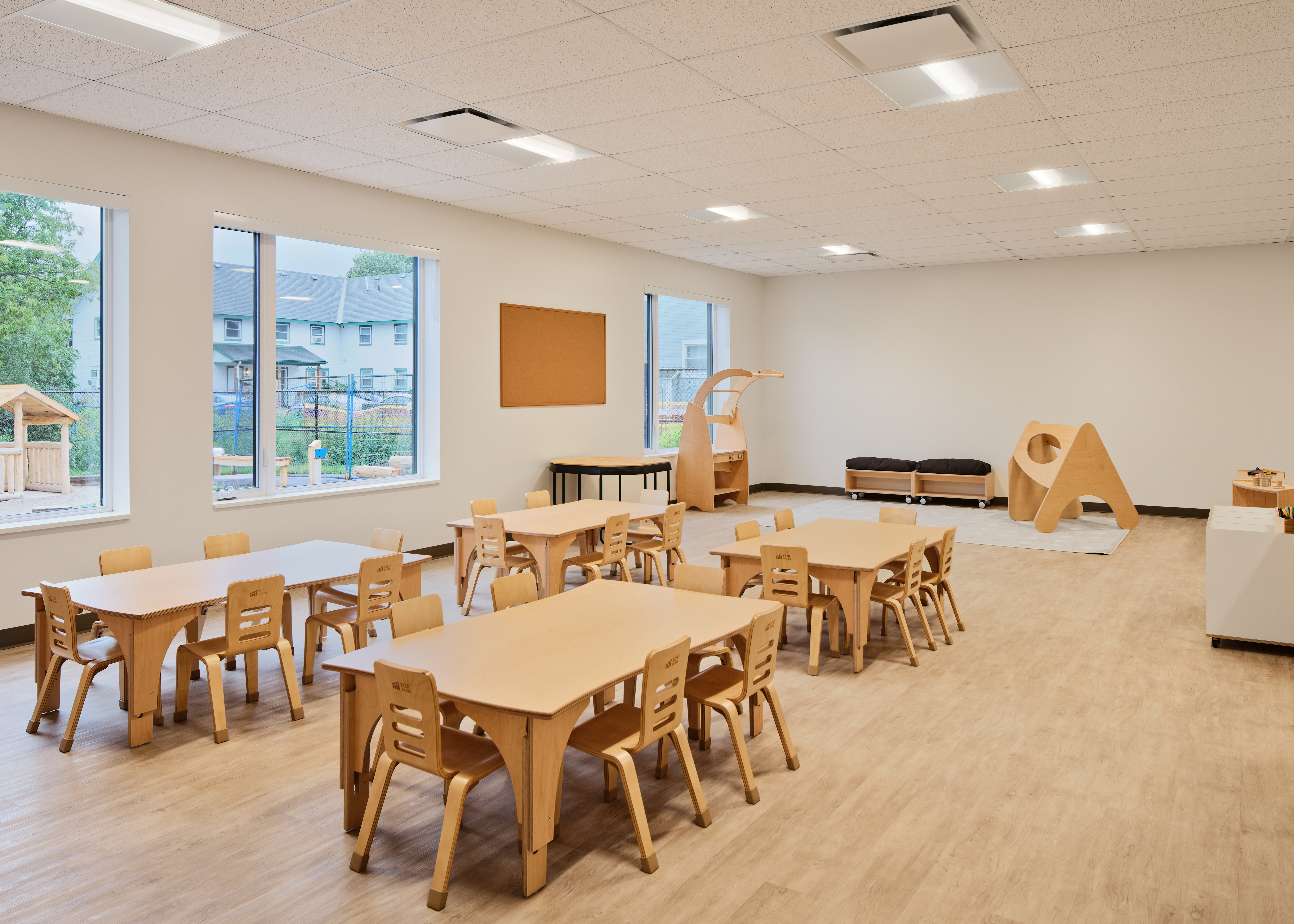 A preschool room with little tables and chairs and large windows.