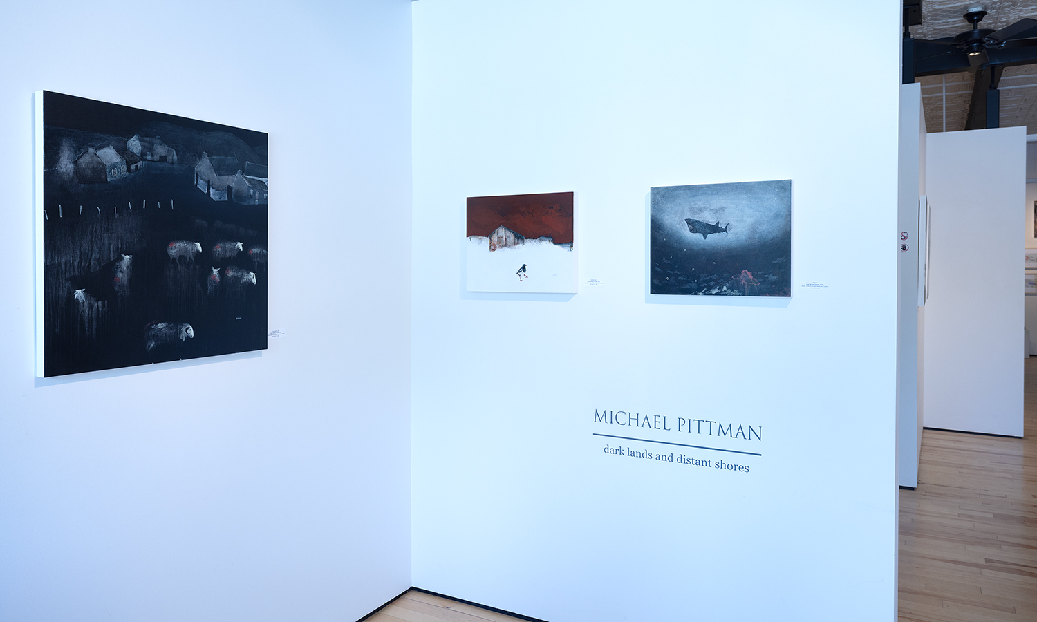 A white wall in a gallery with three pieces of art hanging from it