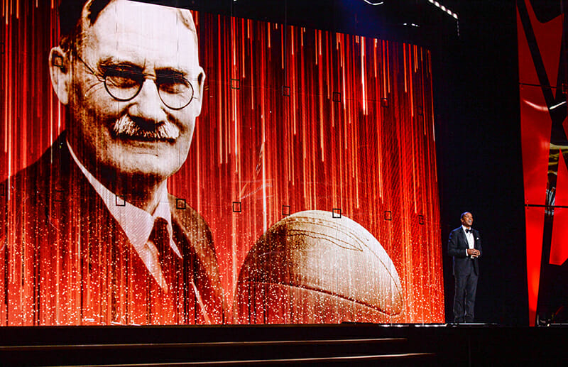 Man speaks in front of a red curtain displaying an image