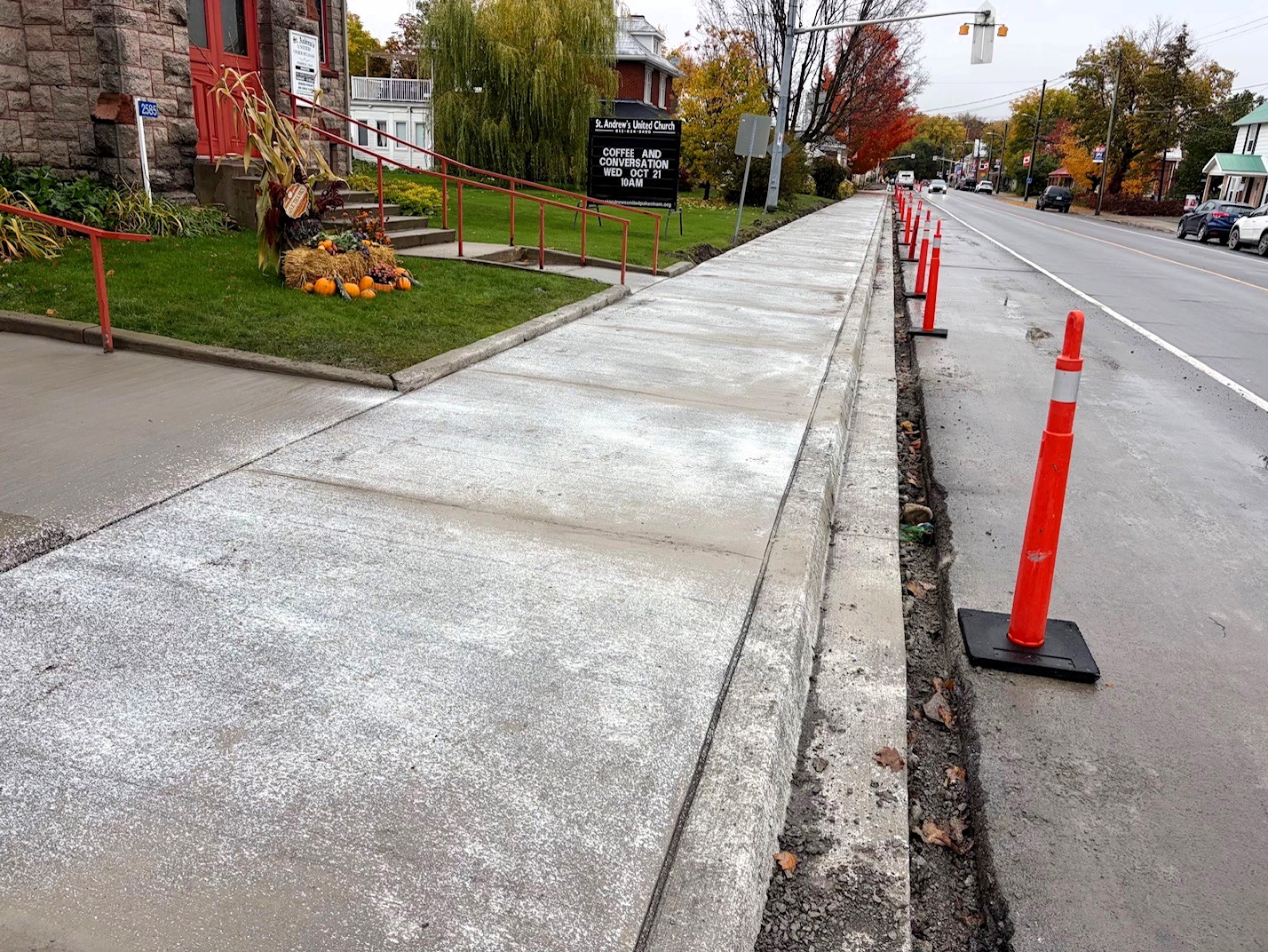 Freshly poured sidewalks on a community street with orange pylons lining the roadway.