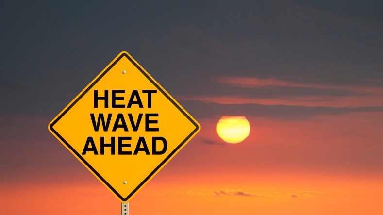 Photo of an orange sky with sun and a yellow triangular sign reading 'Heat Wave Ahead' in black lettering.