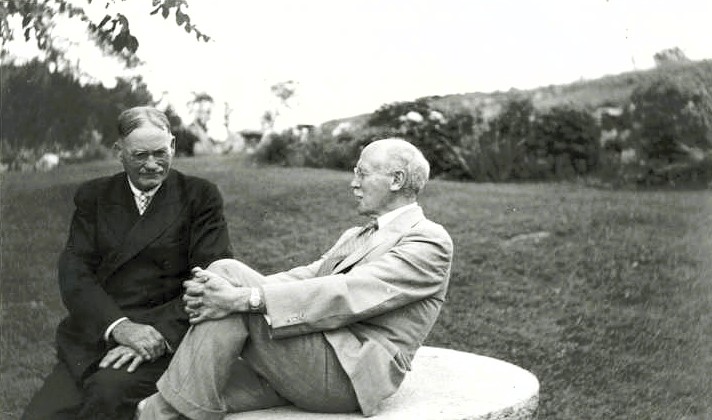 Vintage black and white image of two men sitting on a rock in a rural field