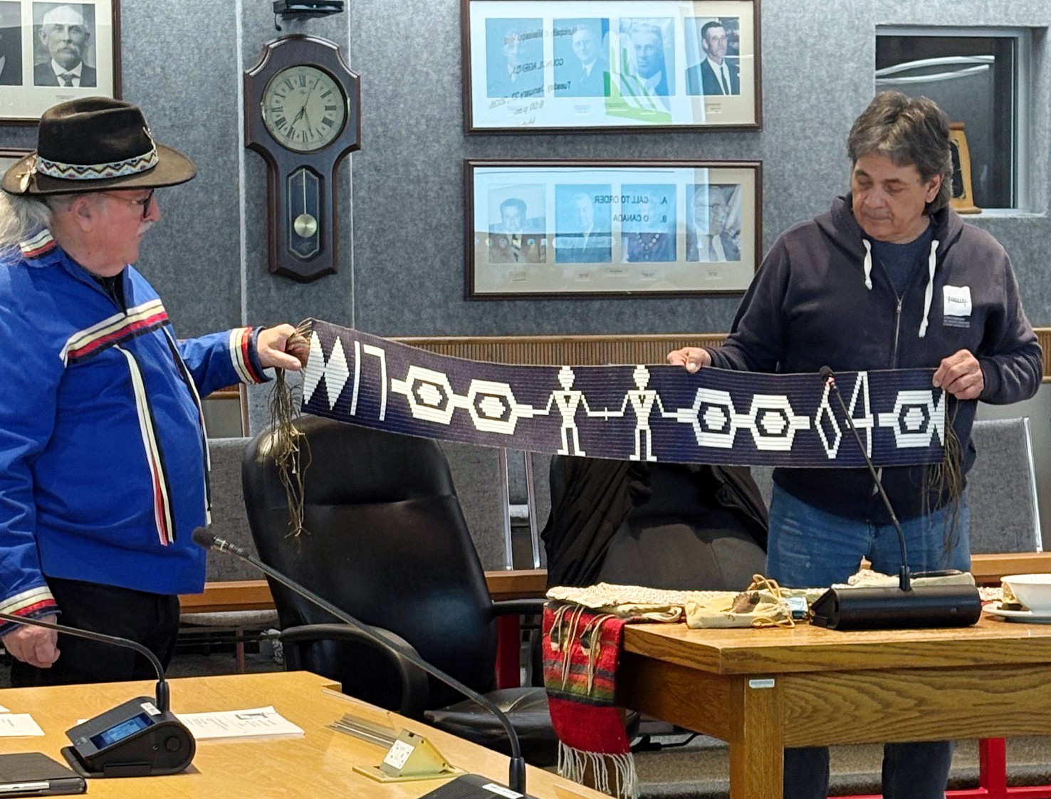 Two men hold up an Indigenous wampum belt